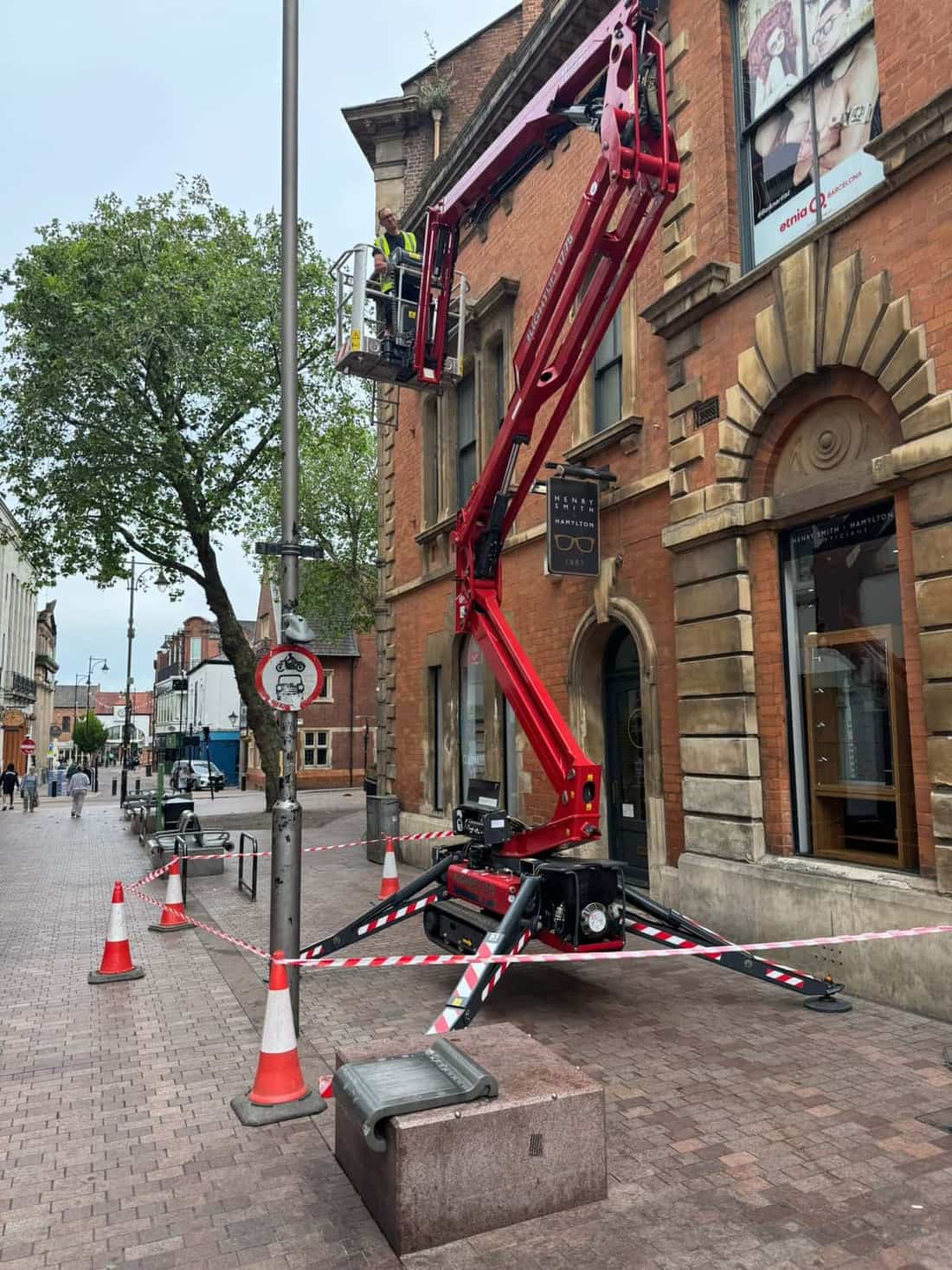 Hinowa Lightlift 17.75 tracked spider lift extended up a town-centre shopfront on Hotel Street, Leicester, with the operative working safely at height
